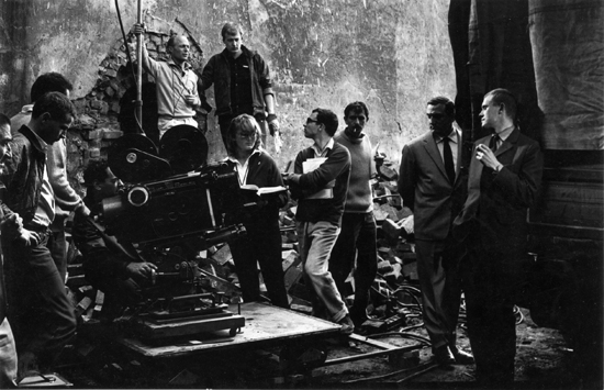 Photo de plateau des "Tontons flingueurs" de Georges Lautner (1963) - Sur le travelling, derrière la caméra Eclair Camé 300, Georges Pastier, cadreur ; en arrière plan, se tenant à un pied de projecteur, Maurice Fellous