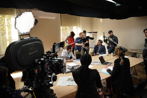 Daylight ambience in a meeting room. - While Julie Conte, first AC, is pulling out her measuring tape, Nicolas Pariser is speaking to the actors. Sebastien, right, standing, lightmeter in hand, awaiting some final measurement. On the far right, Valérie Roucher, assistant director. The little Octaplus is reinforcing the light from the windows while above, you can make out the skirt of black fabric channelling the light from a kino or litemat toplight.